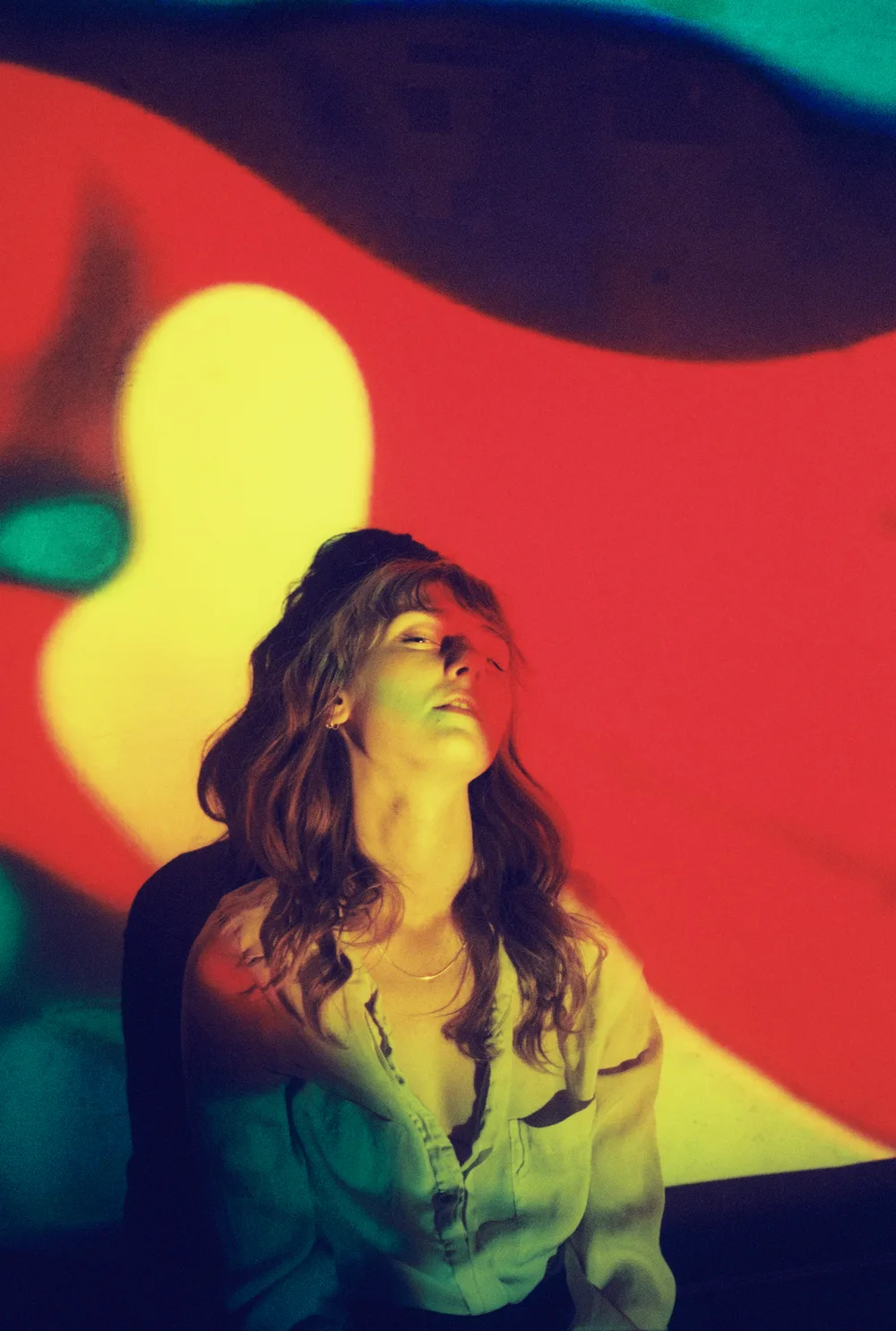 A woman under red and yellow light, head tilted back, on Portra 800, scanned on a Fuji Frontier.