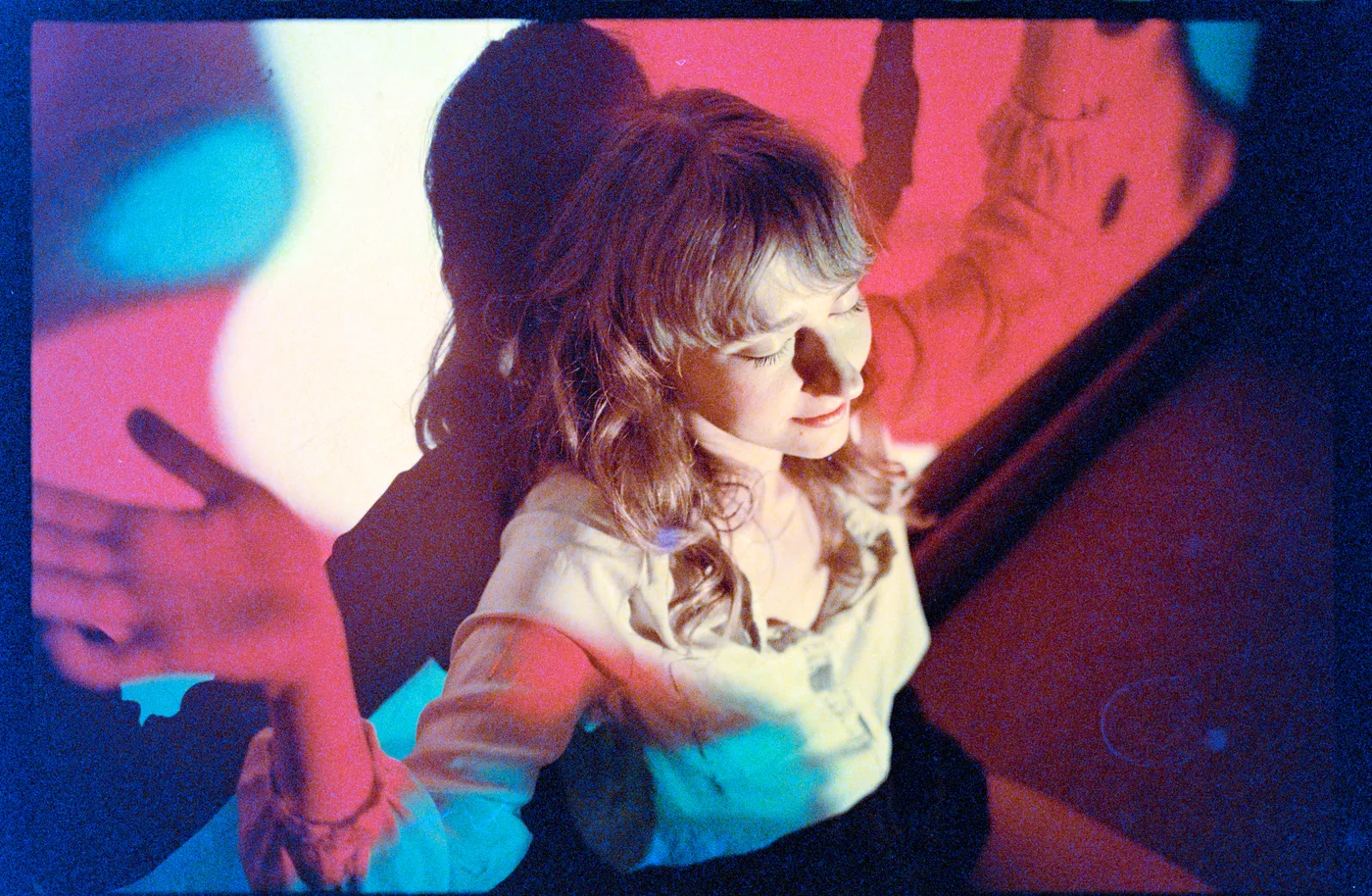 A woman lit by coloured lights, her hand against a wall behind her, on Portra 800, converted by Negative Lab Pro from a white-light raw.